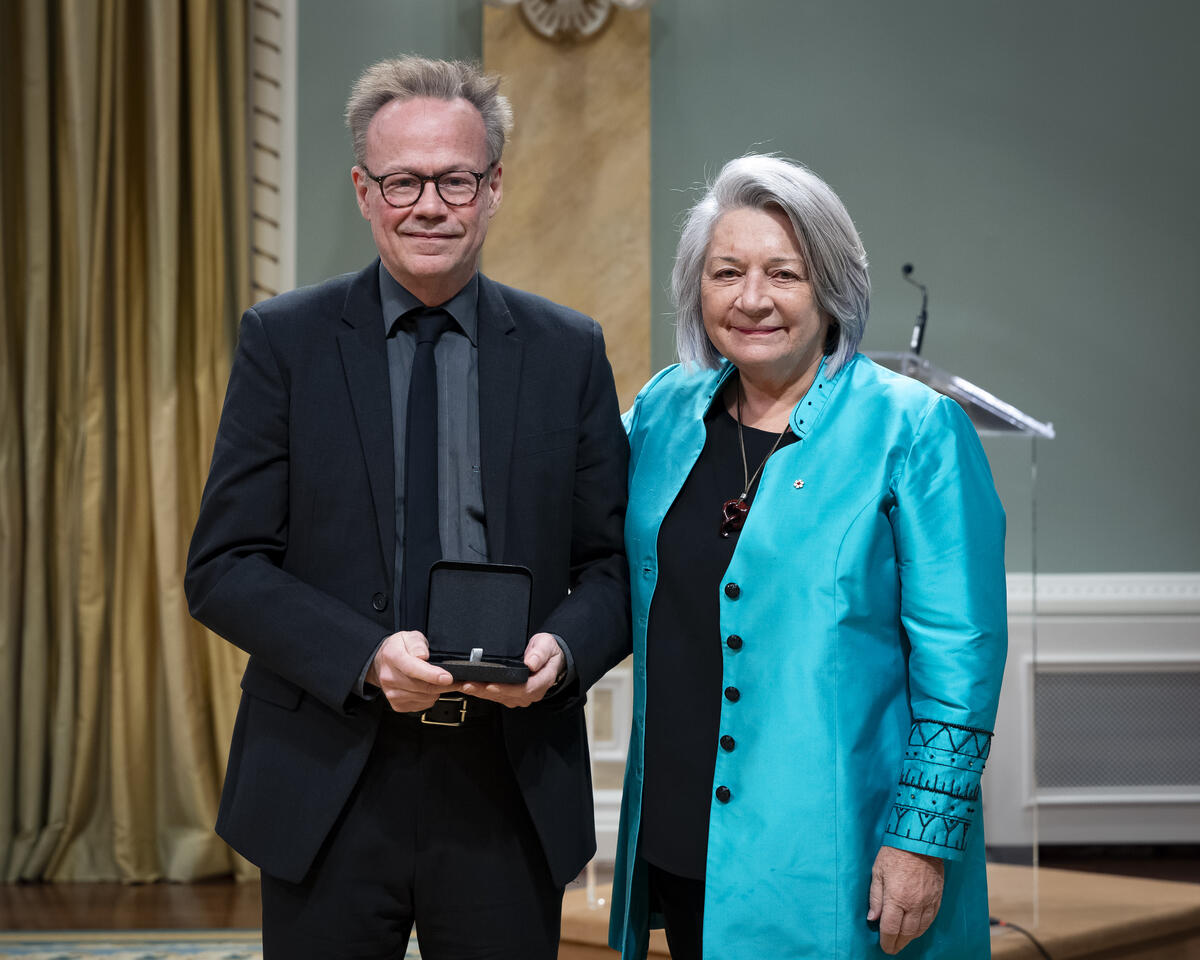 Governor General Mary Simons is posing with a man who is holding an opened award medal case.