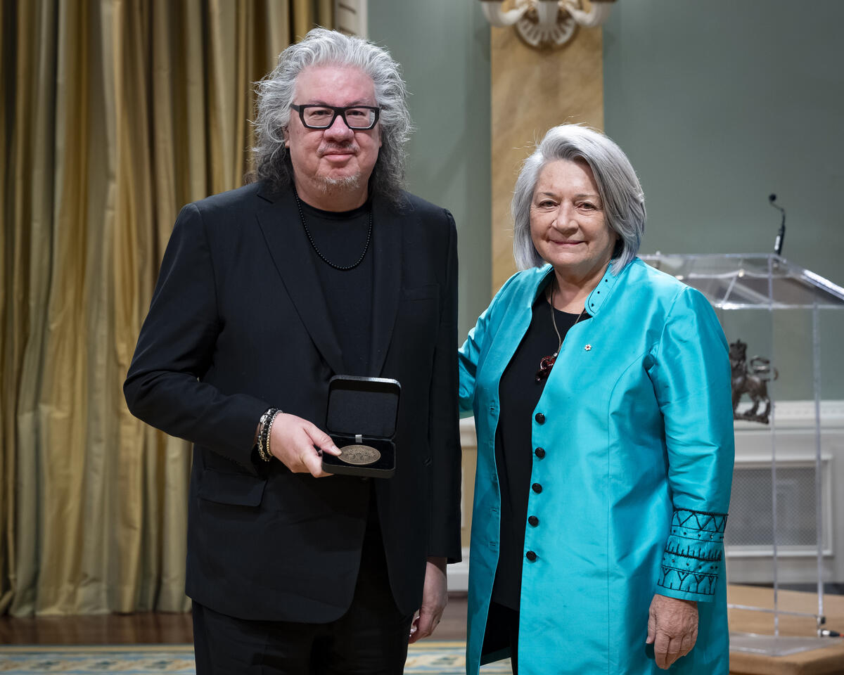 Governor General Mary Simons is posing with a man who is holding an opened award medal case.