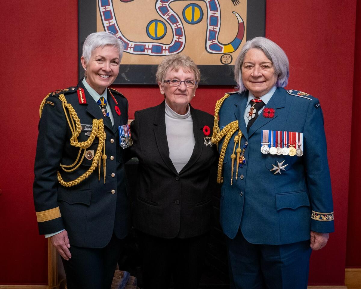 A woman wearing glasses in surrounded by two ladies in uniform. On her left, we see General Jennie Carignan, Chief of the Defence Staff of Canada and on her right, Governor General Mary Simon.