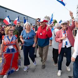 La gouverneure générale Mary Simon et M. Whit Fraser marchent avec une foule de gens à l'extérieur, participant aux festivités de la Fête nationale de l'Acadie.