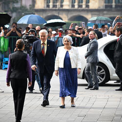 Governor General Mary Simon and Mr. Whit Fraser walking toward Her Excellency Claudia Sheinbaum Pardo, President of the United Mexican States. There is a crowd of onlookers behind barriers. Security personnel and media are present.