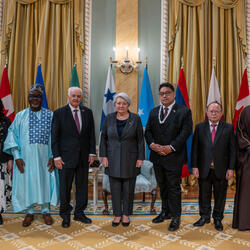 Governor General Simon standing with six&nbsp;new heads of mission, with the flags of each country behind them. Two Ceremonial Guards are in the back.