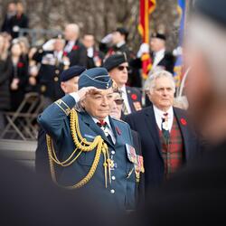 Governor General Mary Simon, wearing the Air Force uniform, is saluting. There is a crowd of people behind her. Her husband Whit Fraser is on her right.