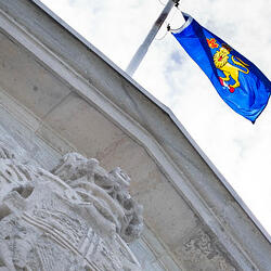 Vue sur le drapeau du gouverneur général au sommet de Rideau Hall. Ciel lumineux avec des nuages blancs.