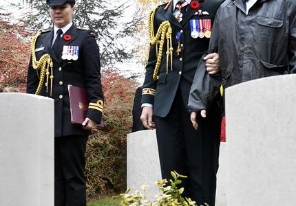 La gouverneure générale du Canada, en uniforme de l'armée canadienne, s'arrête devant une tombe dans un cimetière avec un ancien combattant à ses côtés.
