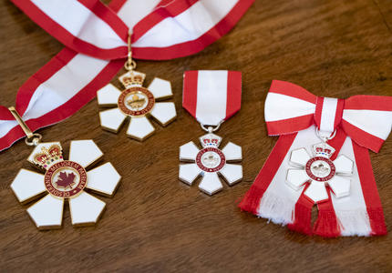 Quatre insignes de l'Ordre du Canada. L'insigne de l'Ordre est un flocon de neige stylisé à six pointes, avec un anneau rouge en son centre qui porte une feuille d'érable stylisée entourée de la devise de l'Ordre.
