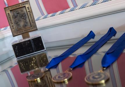 Le trophée du Prix Michener et les trois médailles du Prix Michener, avec des rubans bleus, sont posés sur une table en miroir.