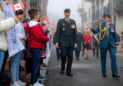 La gouverneure générale Julie Payette, vêtue de l'uniforme des Forces aériennes du Canada, salue des enfants portant de petits drapeaux canadiens sur un trottoir.
