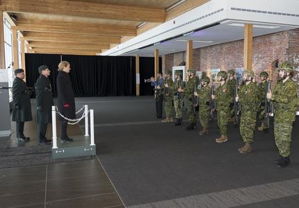 La gouverneure générale Julie Payette est debout sur un dais et regarde une garde de caserne composée de deux rangées de huit réservistes en uniforme de combat.