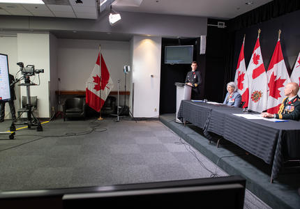 La gouverneure générale Mary Simon est assise à une longue table avec le général Wayne Eyre. Derrière eux, il y a des drapeaux canadiens et des Forces armées canadiennes.