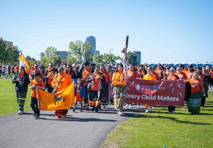 Un groupe de personnes défilant. Beaucoup d'entre eux portent des chandails orange et une grande bannière indiquant "Every Child Matters" est visible.