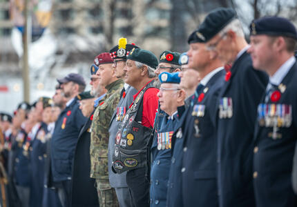 Une rangée de personnes en uniforme se tient devant le Monument commémoratif de guerre du Canada.