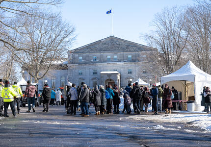 A crowd of people in front of Rideau Hall. There is snow on the ground.