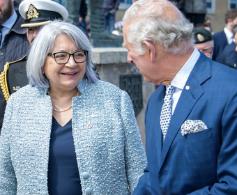 La gouverneure générale Mary Simon, portant une veste bleue, se tient debout devant Sa Majesté le roi Charles III, portant costume bleu marine et d'une cravate bleue. Ils discutent et sourient.