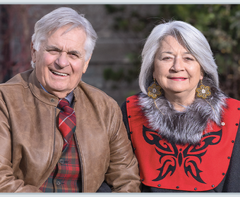 M. Whit Fraser et la gouverneure générale Mary Simon sont assis sur un banc de parc, à l’extérieur. Ils se sourient et se tiennent la main. C’est une journée d’automne ensoleillée.