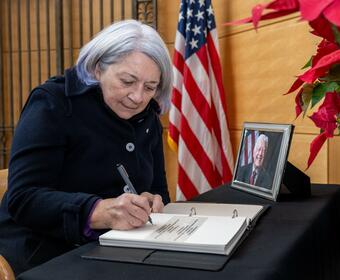 Une femme aux cheveux blancs est assise à une table recouverte d'un tissu noir et signe un livre à côté d'une photo encadrée de l'ancien président américain Jimmy Carter.