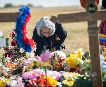 La gouverneure générale Mary Simon dépose quelque chose sur un monticule de fleurs. Il y a une croix floue au premier plan.