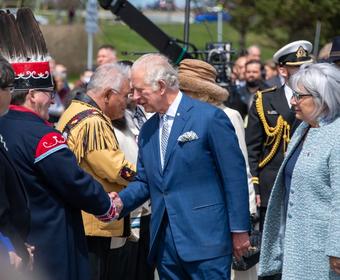Son Altesse Royale le prince de Galles serre la main d'un leader autochtone alors qu'il marche devant une rangée de personnes. La gouverneure générale Simon marche à sa gauche.