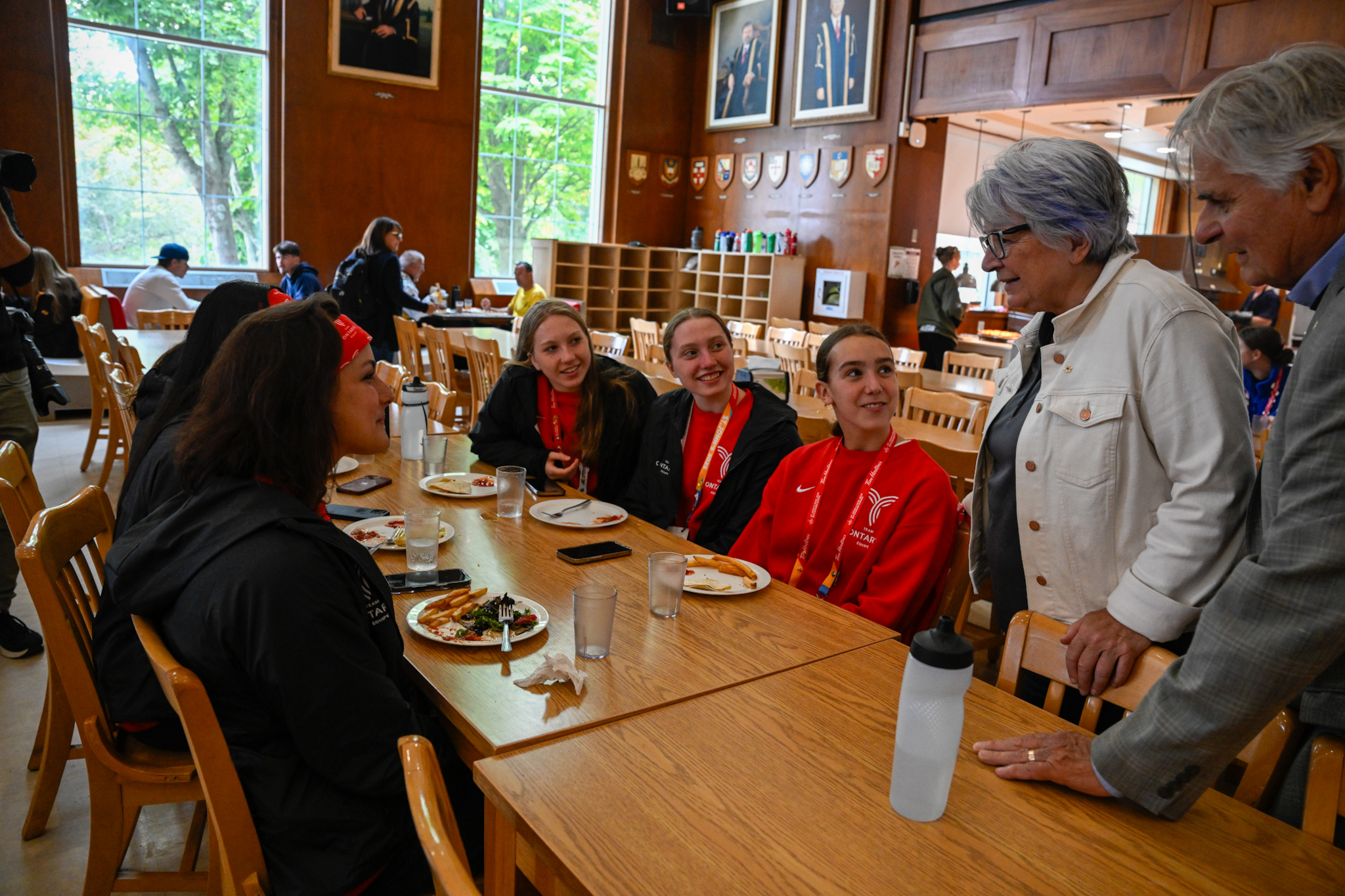Governor General Mary Simon and Mr. Whit Fraser standing, talking to a group of people who are eating breakfast at a large table.